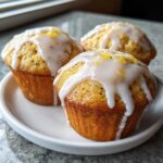 Three delicious Glazed Lemon Poppy Seed Muffins topped with white icing and lemon zest.