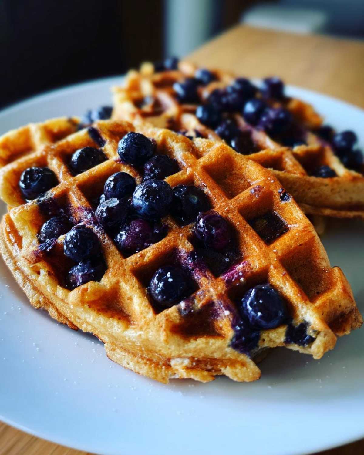 Close-up of two golden Gluten-Free Blueberry Waffles topped generously with fresh blueberries on a white plate.