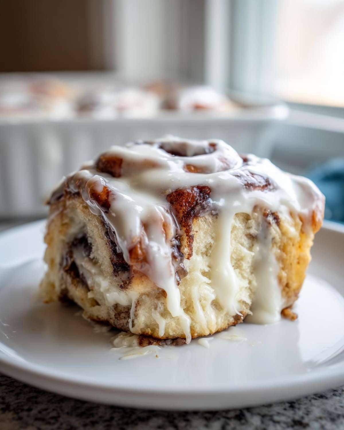Close-up of a single, soft Gluten-Free Cinnamon Roll generously topped with dripping white icing on a white plate.