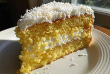 Close-up of a moist slice of Gluten-Free Lemon Coconut Cake layered with cream and topped with shredded coconut.