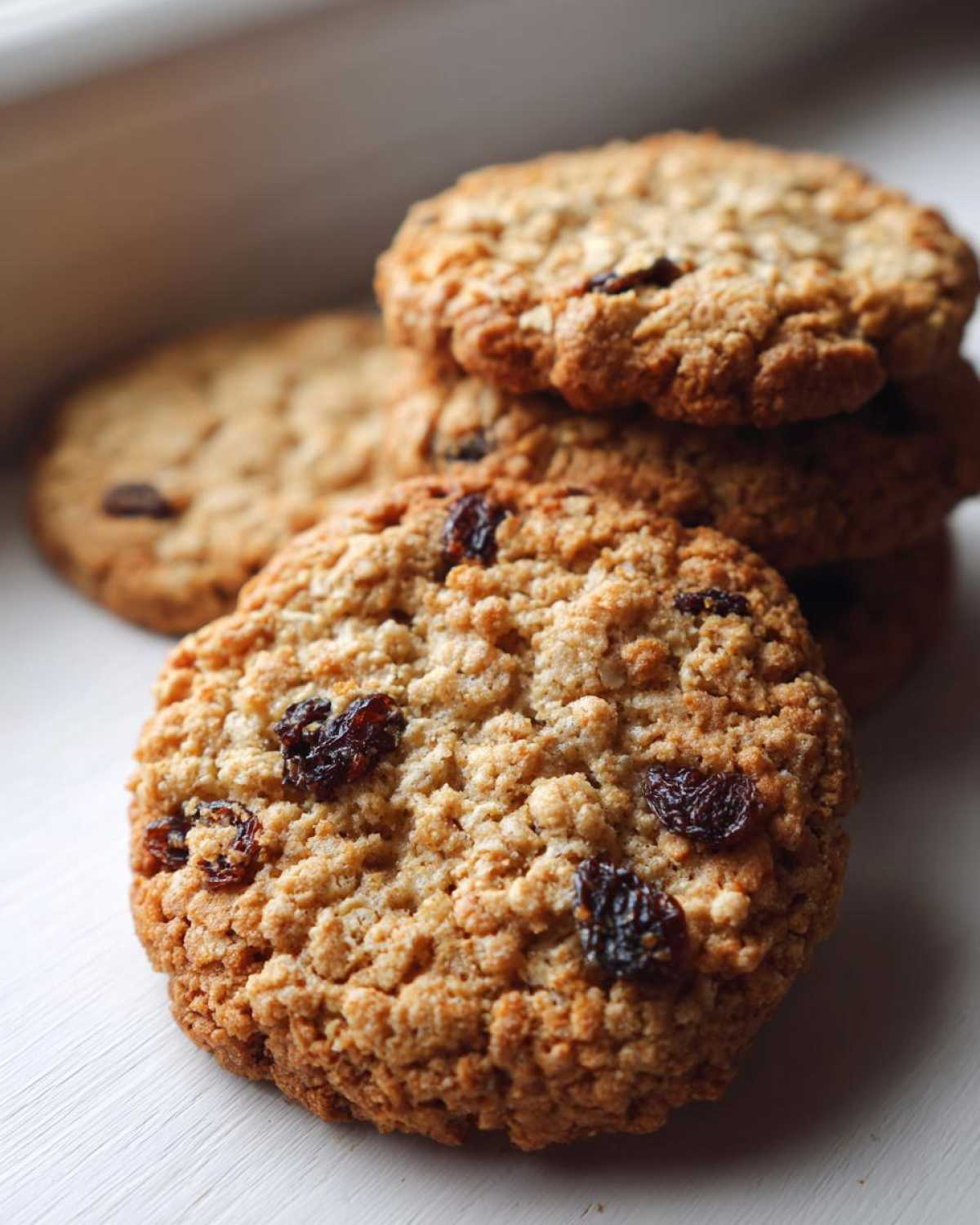Close-up of several golden-brown Gluten-Free Oatmeal Raisin Cookies stacked slightly, featuring visible oats and plump raisins.