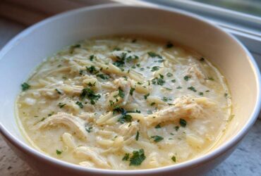 Close-up of a bowl of creamy Greek Lemon Chicken Soup featuring shredded chicken and orzo pasta, garnished with parsley.