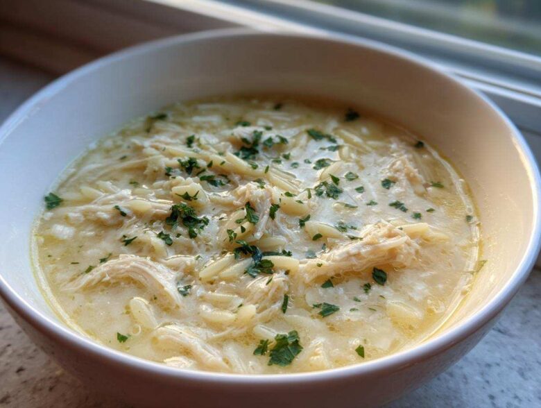 Close-up of a bowl of creamy Greek Lemon Chicken Soup featuring shredded chicken and orzo pasta, garnished with parsley.