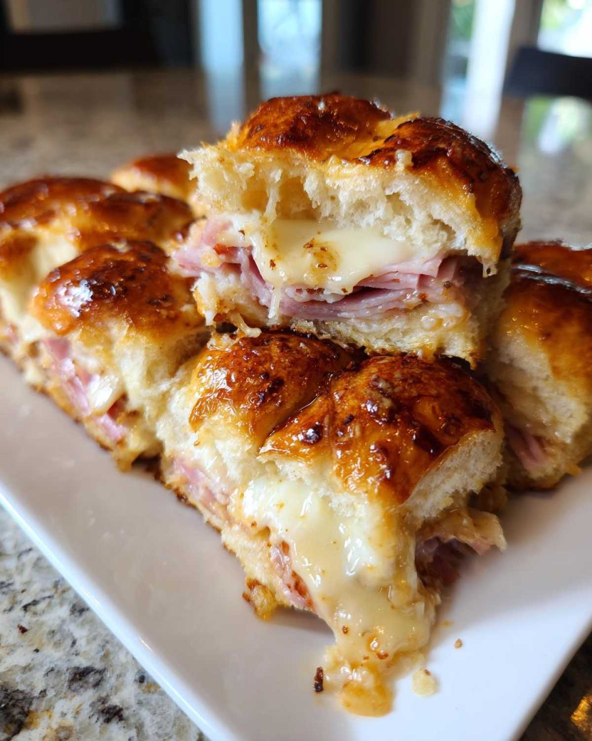 Close-up of Hawaiian Roll Ham and Cheese Sliders with gooey, melted cheese oozing out.