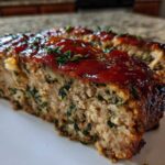 Close-up of a thick slice of Healthy Turkey Spinach Meatloaf topped with a shiny red glaze and fresh parsley.