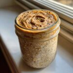 Close-up of High-Protein Peanut Butter Overnight Oats topped with swirled peanut butter and chia seeds in a glass jar.