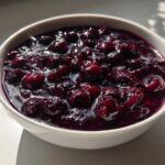 Close-up of thick, rich Homemade Blueberry Syrup with whole berries in a white bowl.