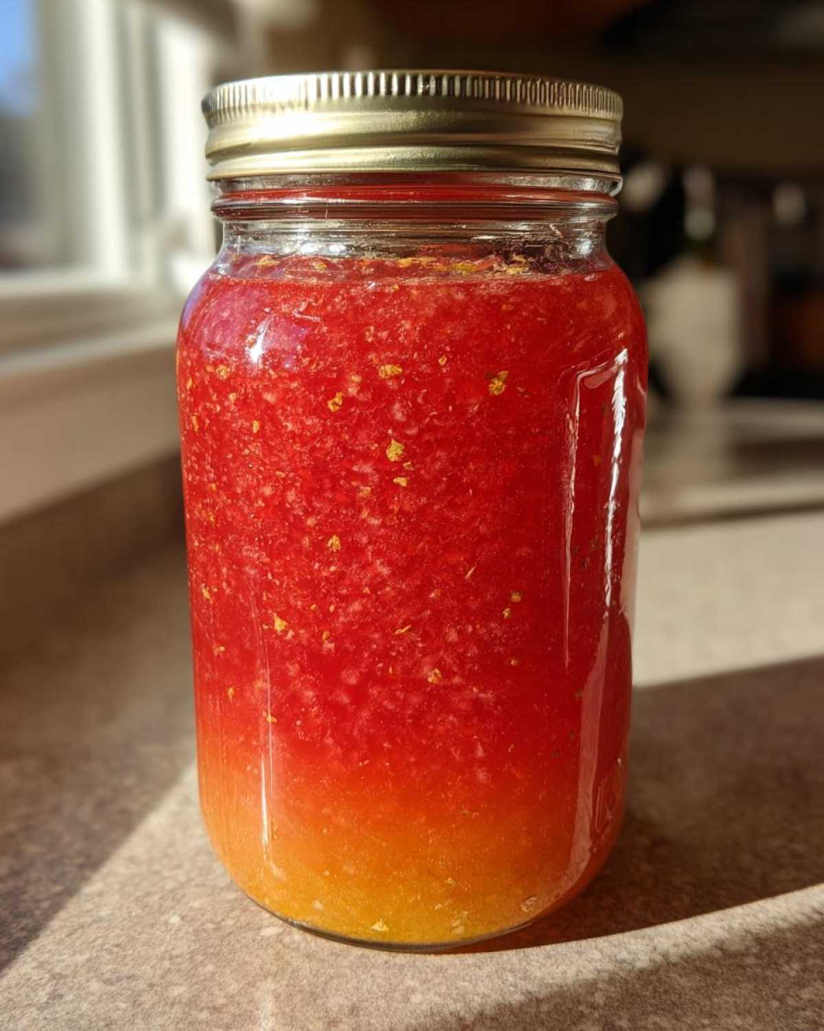 A glass mason jar filled with bright red Homemade Strawberry Lemonade Concentrate, showing separation of liquid.