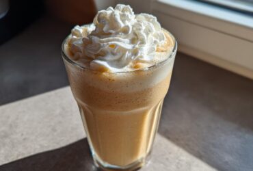 A tall glass filled with a creamy Homemade Vanilla Bean Frappuccino, topped high with whipped cream.