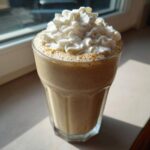A tall glass filled with a frothy Homemade Vanilla Bean Frappuccino topped high with whipped cream.