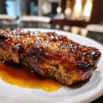 Close-up of a thick, caramelized Honey Glazed Ham Steak in the Skillet, glistening with sauce on a white plate.