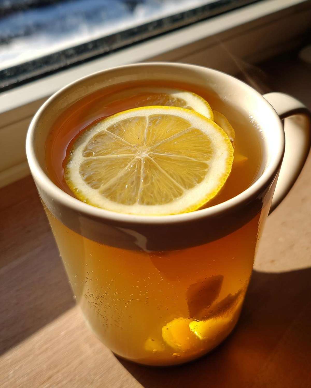 Close-up of steaming Honey Lemon Ginger Tea in a mug, topped with bright lemon slices.