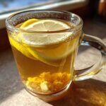 Close-up of a glass mug filled with warm Honey Lemon Ginger Tea, featuring lemon slices and ginger pieces.