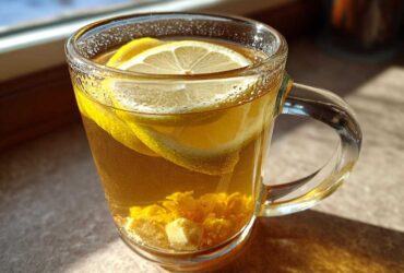 Close-up of a glass mug filled with warm Honey Lemon Ginger Tea, featuring lemon slices and ginger pieces.