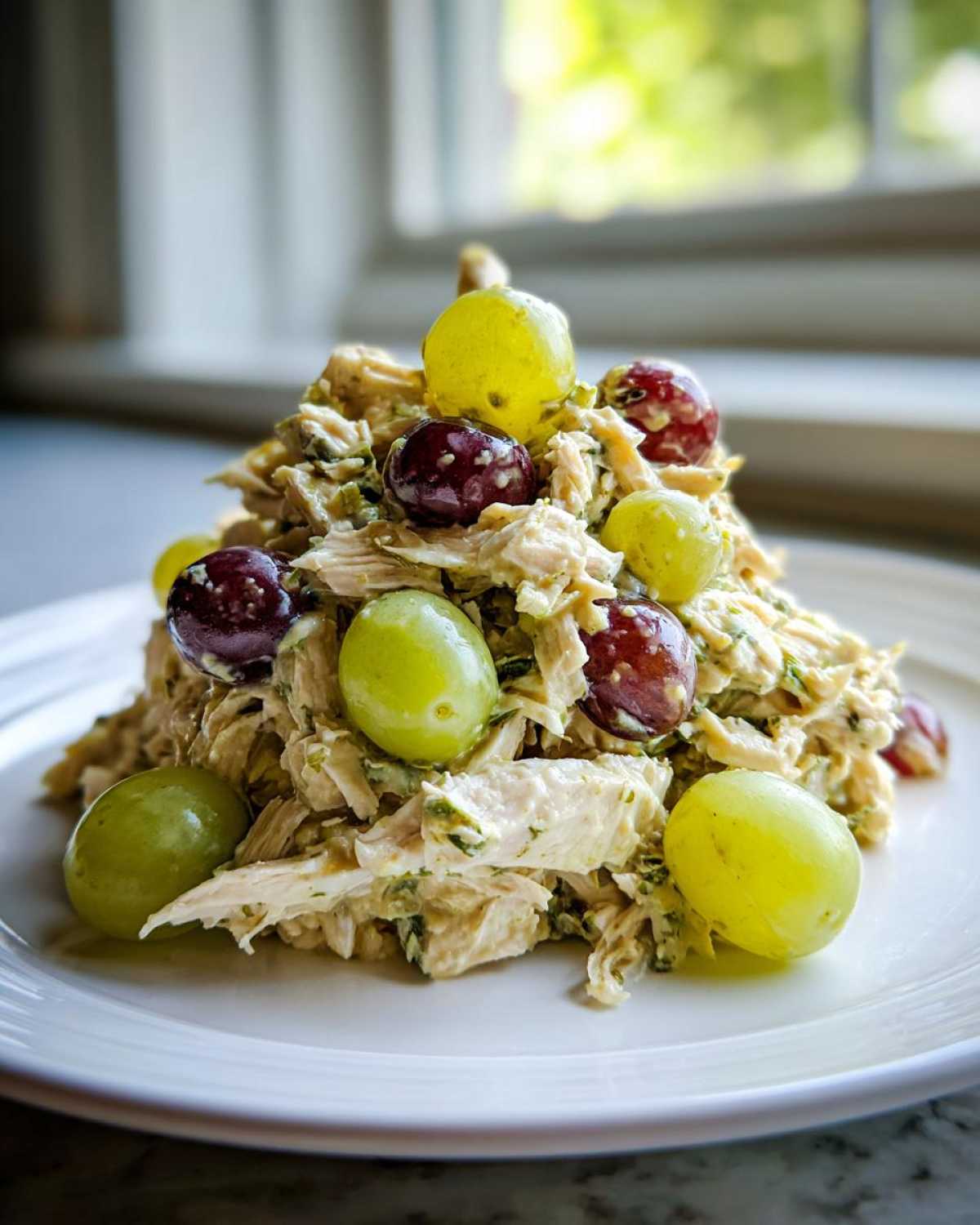 A mound of Honey Mustard Chicken Salad with Grapes, garnished with whole green and red grapes, served on a white plate.