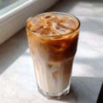 A tall glass filled with a layered Iced Brown Sugar Oatmilk Latte, showing rich espresso mixing with white oatmilk over ice.
