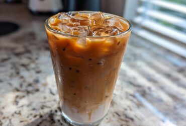 A tall, sweating glass filled with a layered Iced Brown Sugar Oatmilk Latte, topped with ice cubes.