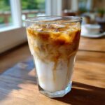 Close-up of an Iced Honey Almond Milk Latte showing rich espresso swirling into the white almond milk and ice.