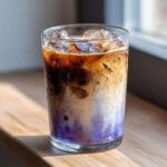 Close-up of a tall glass containing an Iced Lavender Latte with distinct purple, white, and dark coffee layers over ice.