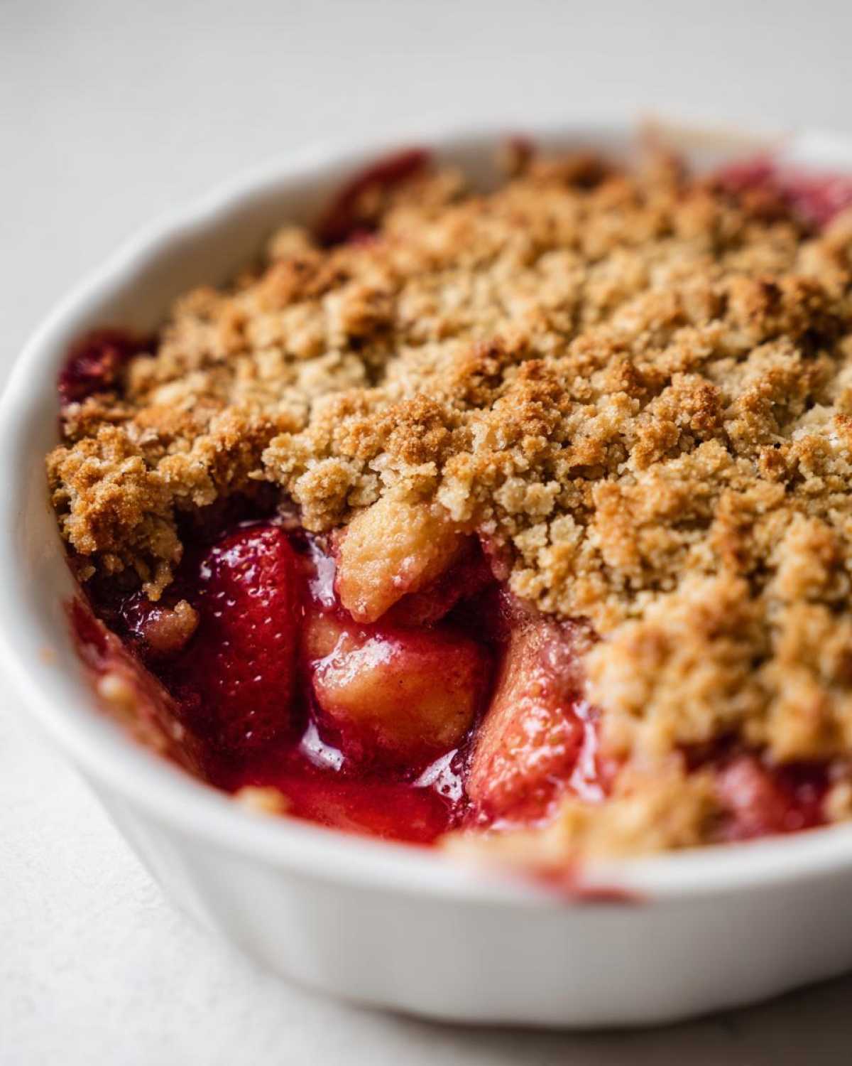 Close-up of a warm, individual serving of Strawberry Rhubarb Crisp with bubbling red fruit filling and golden brown topping.