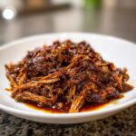 Close-up of rich, saucy shredded Instant Pot Beef Barbacoa piled on a white plate.