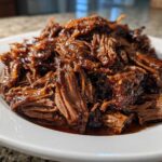 A mound of rich, saucy, shredded Instant Pot Beef Barbacoa served on a white plate.