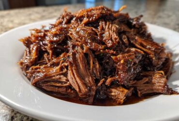 A mound of rich, saucy, shredded Instant Pot Beef Barbacoa served on a white plate.