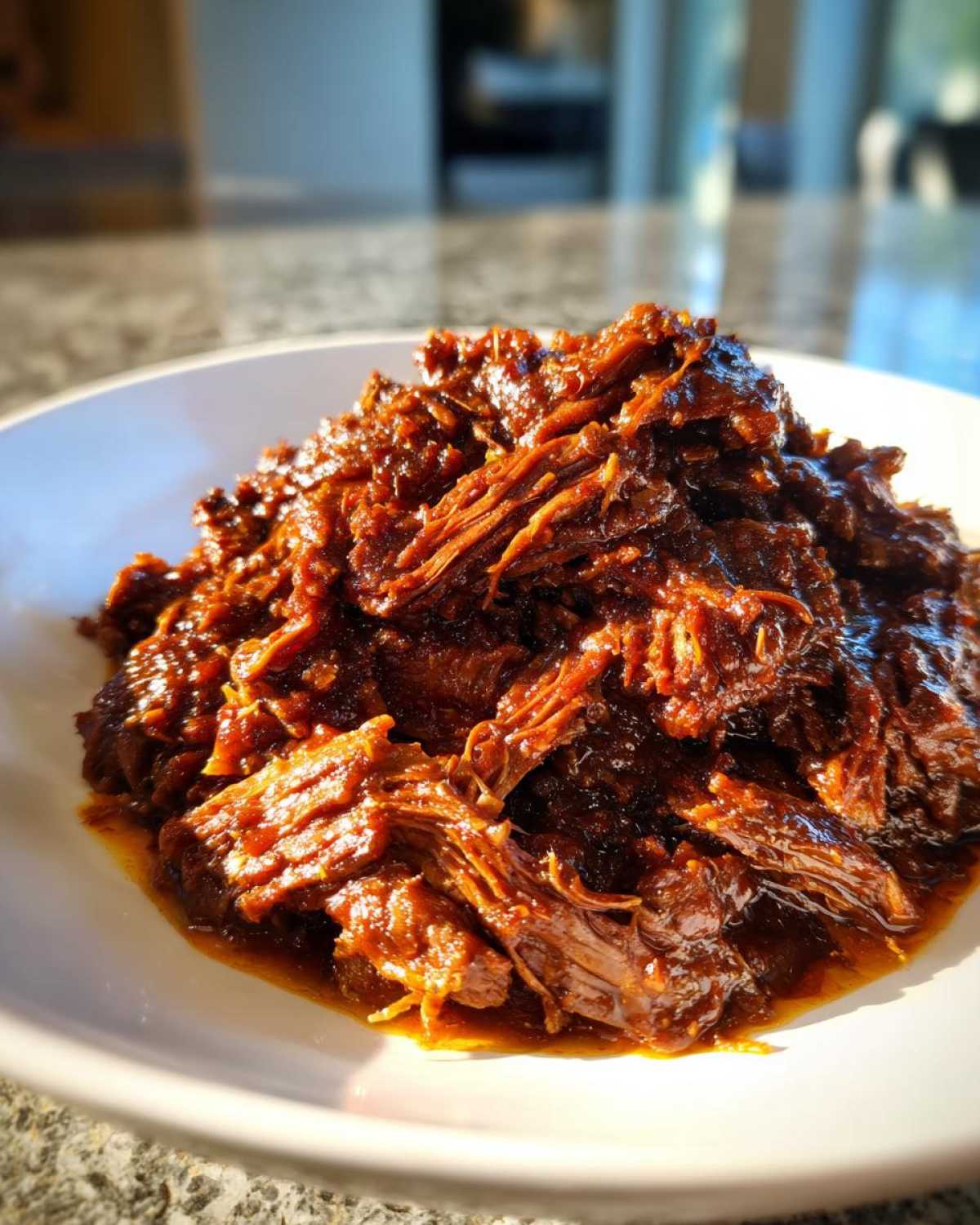 Close-up of rich, shredded Instant Pot Beef Barbacoa coated in savory sauce on a white plate.