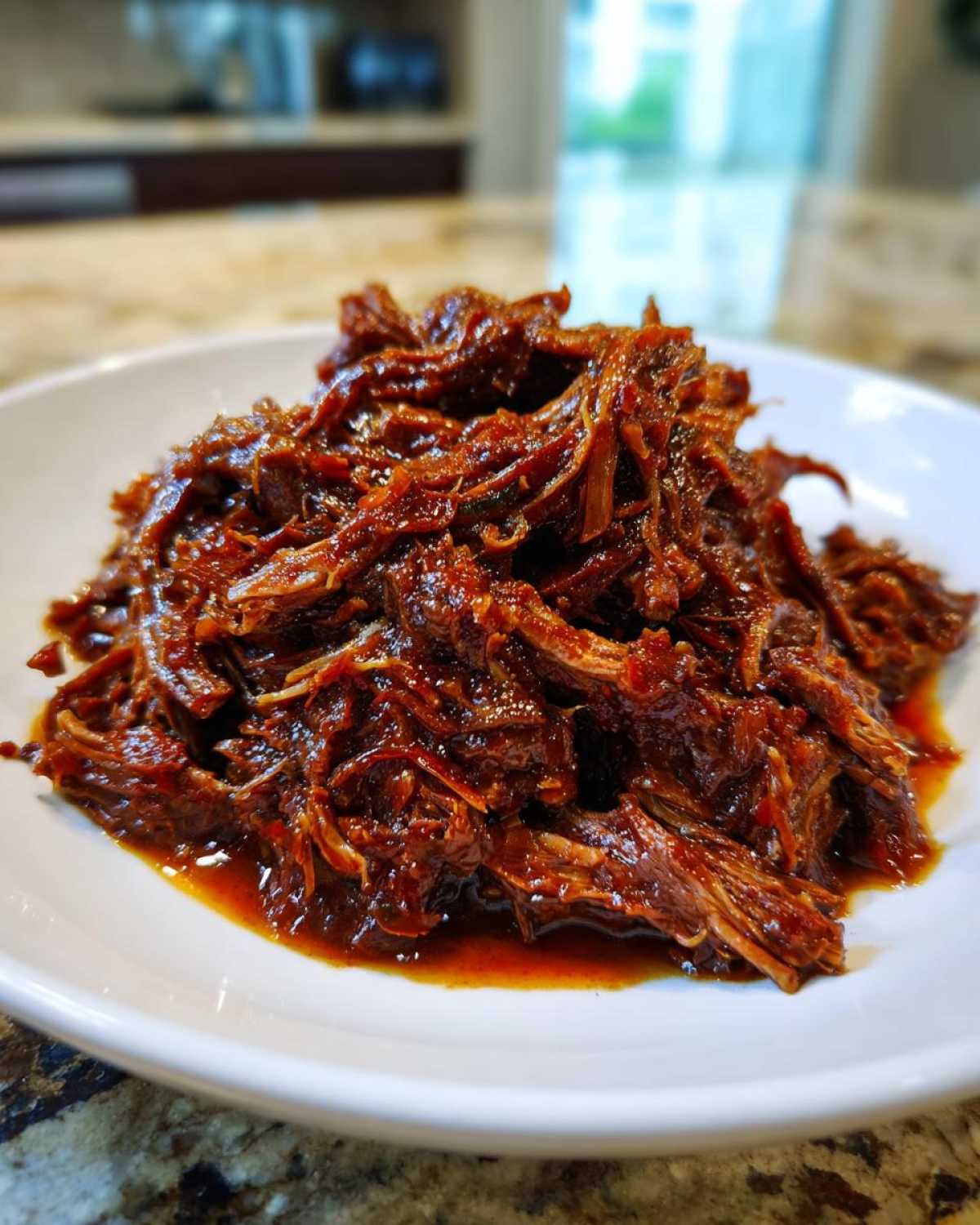 Close-up of rich, shredded Instant Pot Beef Barbacoa piled high on a white plate.