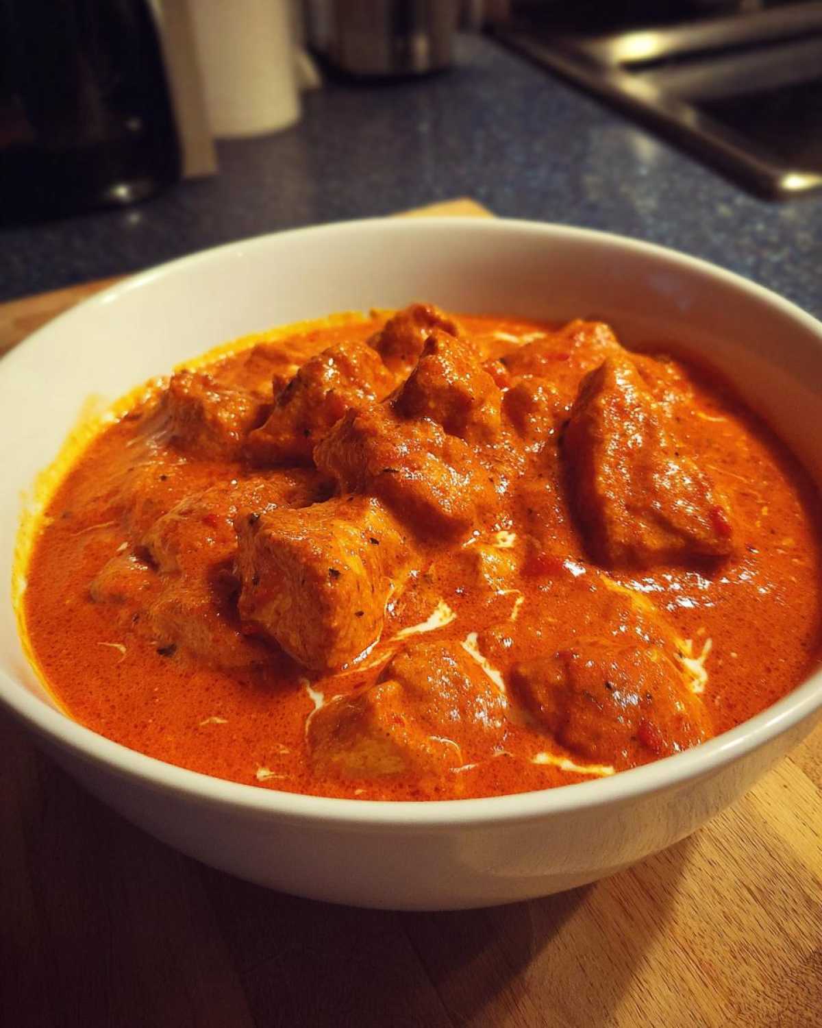 Close-up of a white bowl filled with vibrant orange Instant Pot Butter Chicken, showing creamy sauce and tender chicken pieces.