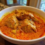 Close-up of creamy, orange-red Instant Pot Butter Chicken pieces served in a white bowl.