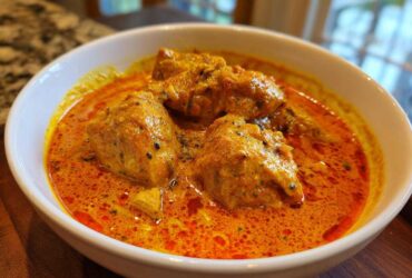 Close-up of creamy, orange-red Instant Pot Butter Chicken pieces served in a white bowl.