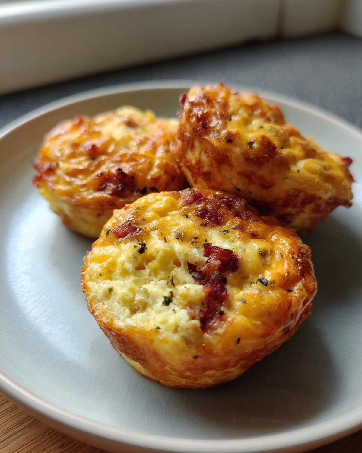 Three golden-brown Keto Bacon and Egg Muffins served on a light blue plate.