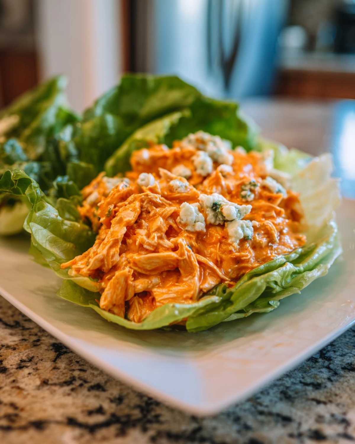 A single serving of Keto Buffalo Chicken Lettuce Wraps filled with orange buffalo chicken salad and topped with blue cheese.