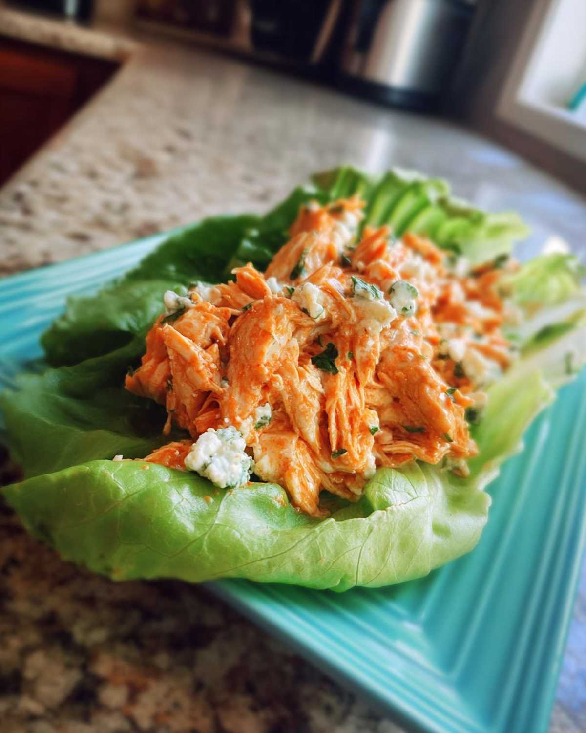 A single serving of Keto Buffalo Chicken Lettuce Wraps featuring shredded orange buffalo chicken mixture topped with blue cheese crumbles in a crisp lettuce cup.