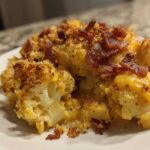 A close-up serving of Keto Cauliflower Mac and Cheese topped with crispy bacon bits and a golden crust.