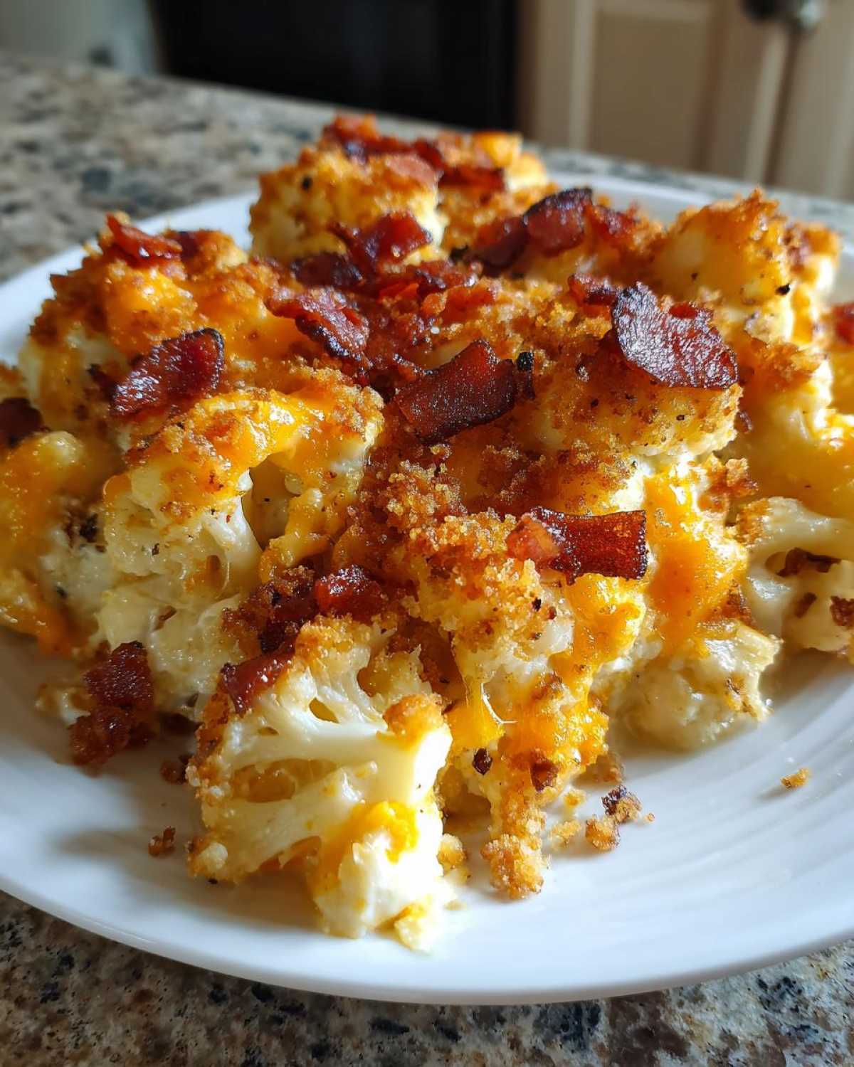 Close-up of Keto Cauliflower Mac and Cheese topped with melted cheddar and crispy bacon bits on a white plate.