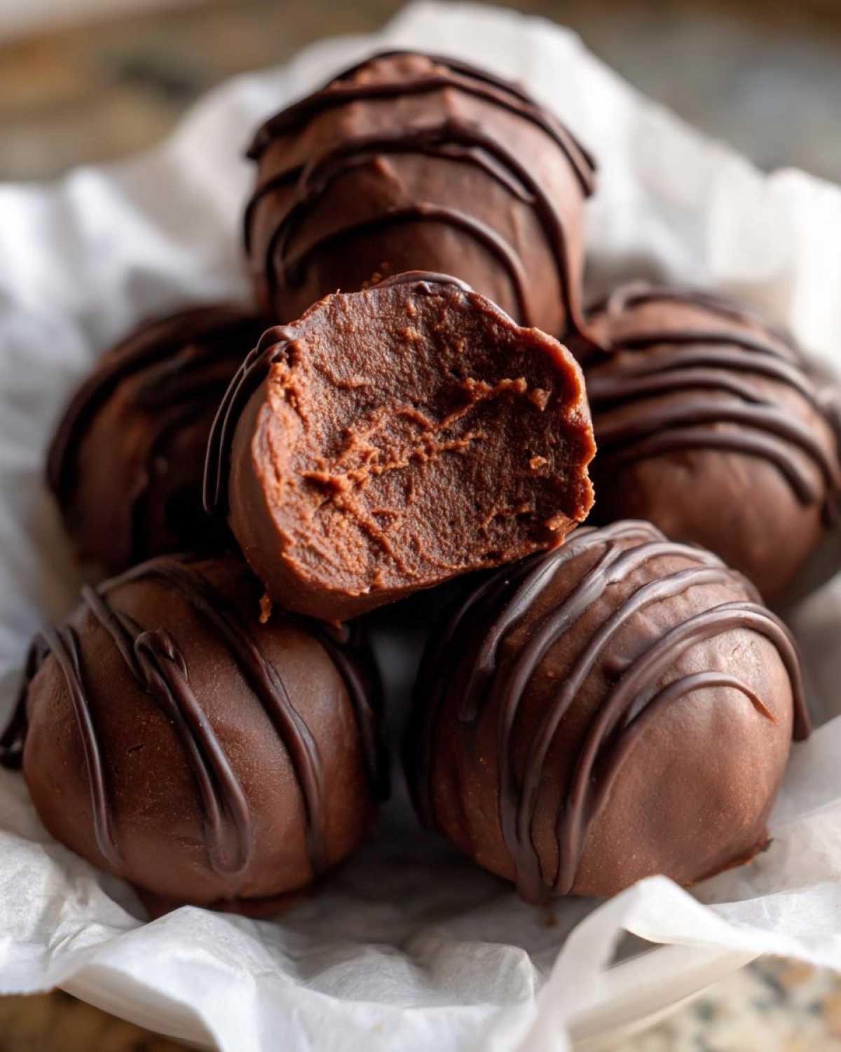 Close-up of rich chocolate Keto Chocolate Peanut Butter Fat Bombs, one bitten to show the creamy interior.