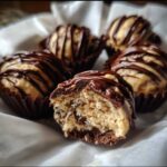 A close-up of several Keto Chocolate Peanut Butter Fat Bombs, one bitten open showing the creamy interior and chocolate drizzle.