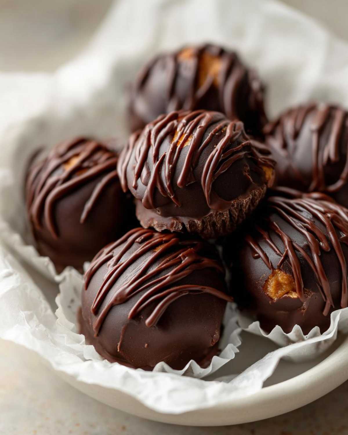 A close-up of several rich, dark chocolate covered Keto Chocolate Peanut Butter Fat Bombs drizzled with more chocolate.