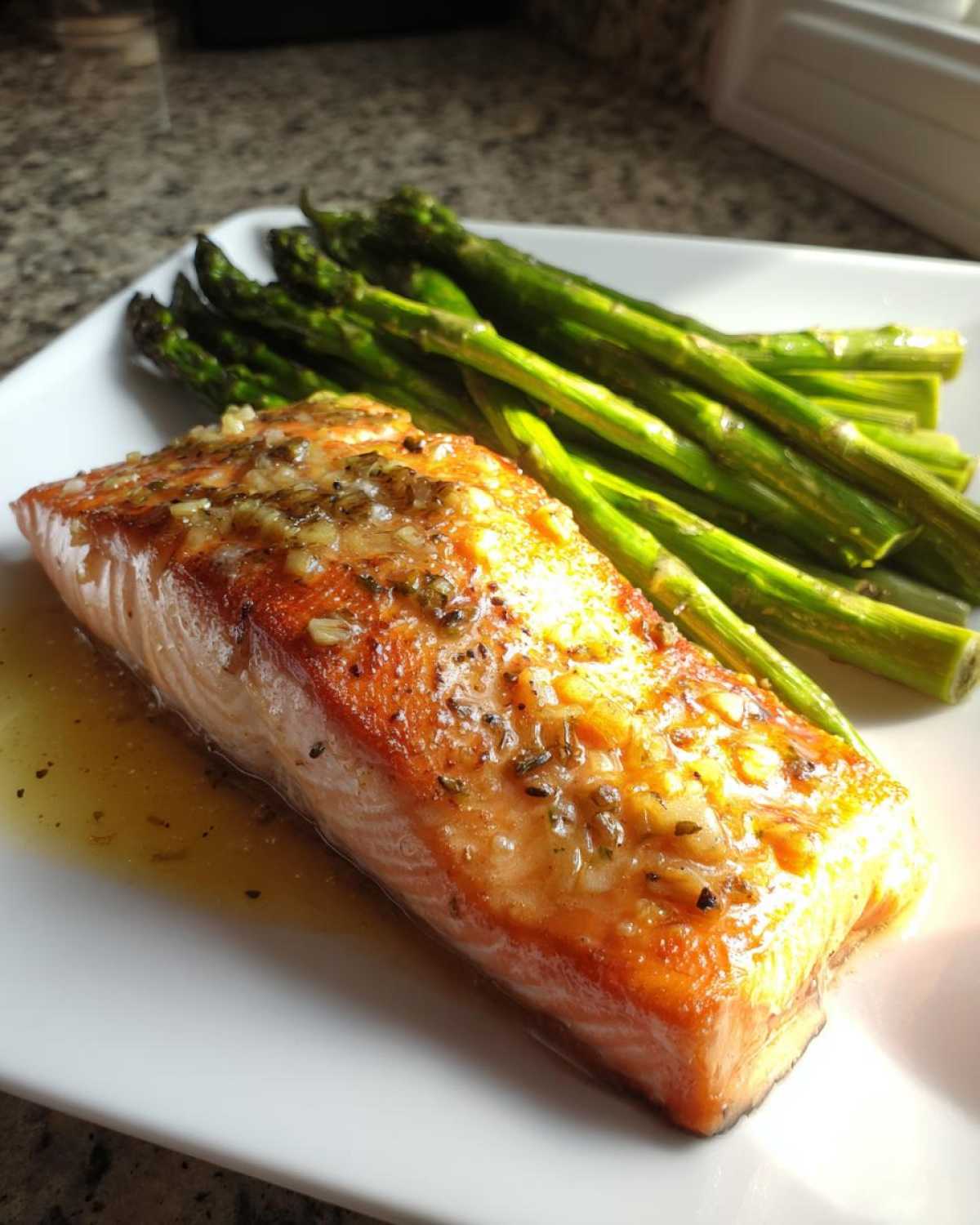 A perfectly cooked fillet of Keto Garlic Butter Salmon topped with garlic butter sauce, served alongside roasted asparagus.