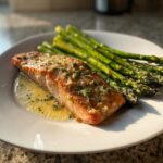 A perfectly cooked fillet of Keto Garlic Butter Salmon topped with garlic and herbs, served alongside roasted asparagus.
