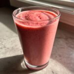 Close-up of a thick, pink Keto Strawberry Cheesecake Smoothie served in a tall glass, catching sunlight.