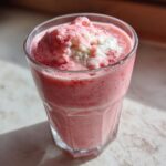 Close-up of a vibrant pink Keto Strawberry Cheesecake Smoothie topped with a dollop of white cream.