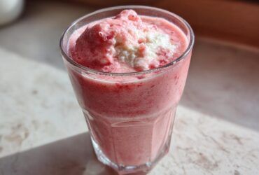 Close-up of a vibrant pink Keto Strawberry Cheesecake Smoothie topped with a dollop of white cream.