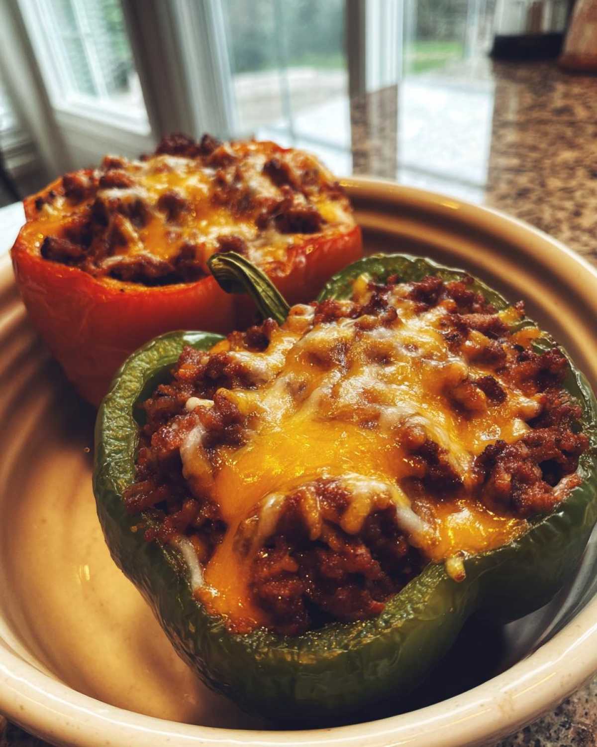 Two Keto Taco Stuffed Peppers, one green and one red, topped with melted cheddar cheese.