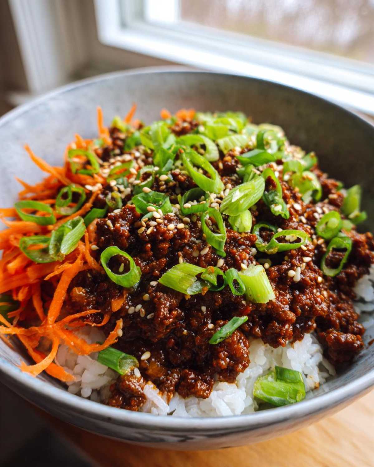 A close-up of Korean Ground Beef Bulgogi Bowls featuring savory ground beef over rice, topped with shredded carrots, green onions, and sesame seeds.