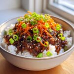 A bowl of Korean Ground Beef Bulgogi Bowls featuring saucy ground beef over white rice, topped with shredded carrots and green onions.