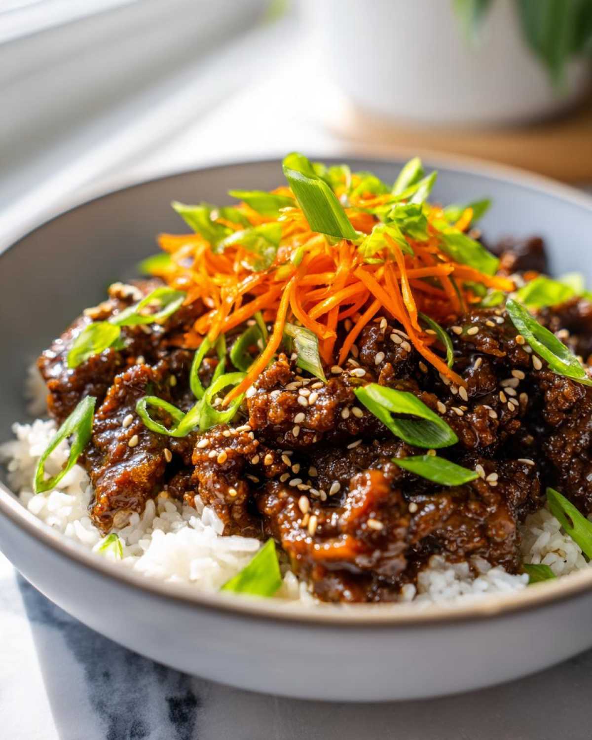 Close-up of Korean Ground Beef Bulgogi Bowls served over white rice, topped with shredded carrots and green onions.