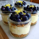 Four individual Lemon Blueberry Cheesecake Jars topped with fresh blueberries and lemon zest.